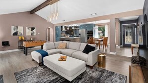 A spacious living room with a large sectional sofa, a foosball table, and a kitchen in the background. - The Sinatra - Fun, 5BD Home! Huge Pool! Game Room! (Round Rock)