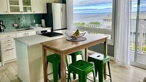 A modern kitchen with a large island, green bar stools, and a view of the ocean.