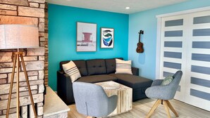 A living room with a teal wall, a stone accent wall, a grey sofa, a wooden coffee table, a grey armchair, and a guitar.