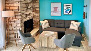 A living room with a stone fireplace, teal walls, a brown sofa with patterned cushions, two grey armchairs, and a wooden coffee table.