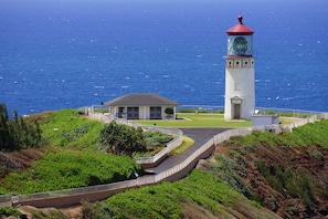 A lighthouse with a red roof and a white tower, surrounded by a landscaped area with a pathway and a small building.