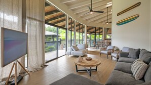 A spacious living room with a large window, a ceiling fan, and a modern sofa set. - Stylish and Spacious Condo - A/C in 2 Bedrooms, Huge Lanai, Great Location (Princeville)