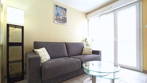 Een woonkamer met een grijze bank, een glazen salontafel en een poster aan de muur.