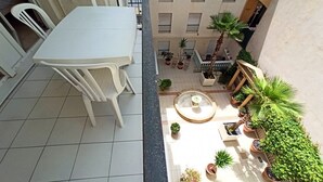 Een binnenplaats met een witte tafel en stoelen, omringd door potplanten en een kleine fontein.