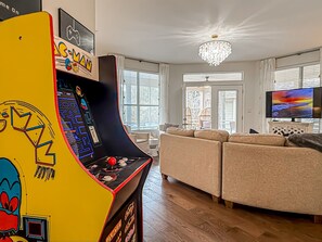 A living room with a large sofa, a television, and a colorful arcade machine. - BayPine Two Golf Carts | Sandestin Heated Pools |Bunk Room Message 4 SNOWBIRD JAN (Miramar Beach)