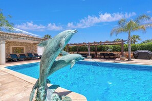 A swimming pool with a dolphin sculpture, lounge chairs, and a pergola with umbrellas.