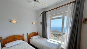 Ein Zimmer mit zwei Betten, einem Deckenventilator, einem Fenster mit Vorhängen und Meerblick.