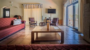 Un salón amplio con un sofá rojo, dos sillones de cuero, una mesa de centro de madera y un ventanal con vistas al exterior.