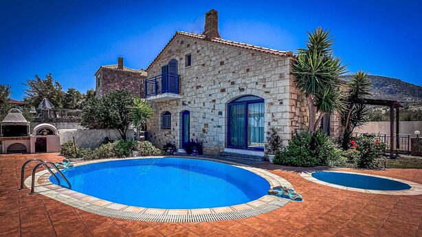 Una villa de piedra con piscina, zona de barbacoa y jardín con palmeras.