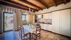 Una cocina con vigas de madera, una mesa de comedor con sillas y un ventanal con cortinas.