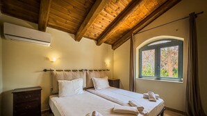 Cama doble con ropa de cama y toallas blancas, cabecera de madera, dos mesitas de noche, una ventana con cortinas y techo de madera.