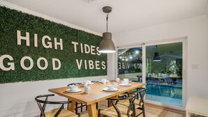 Zona pranzo con tavolo in legno, sedie nere e parete decorata con piante e scritte.