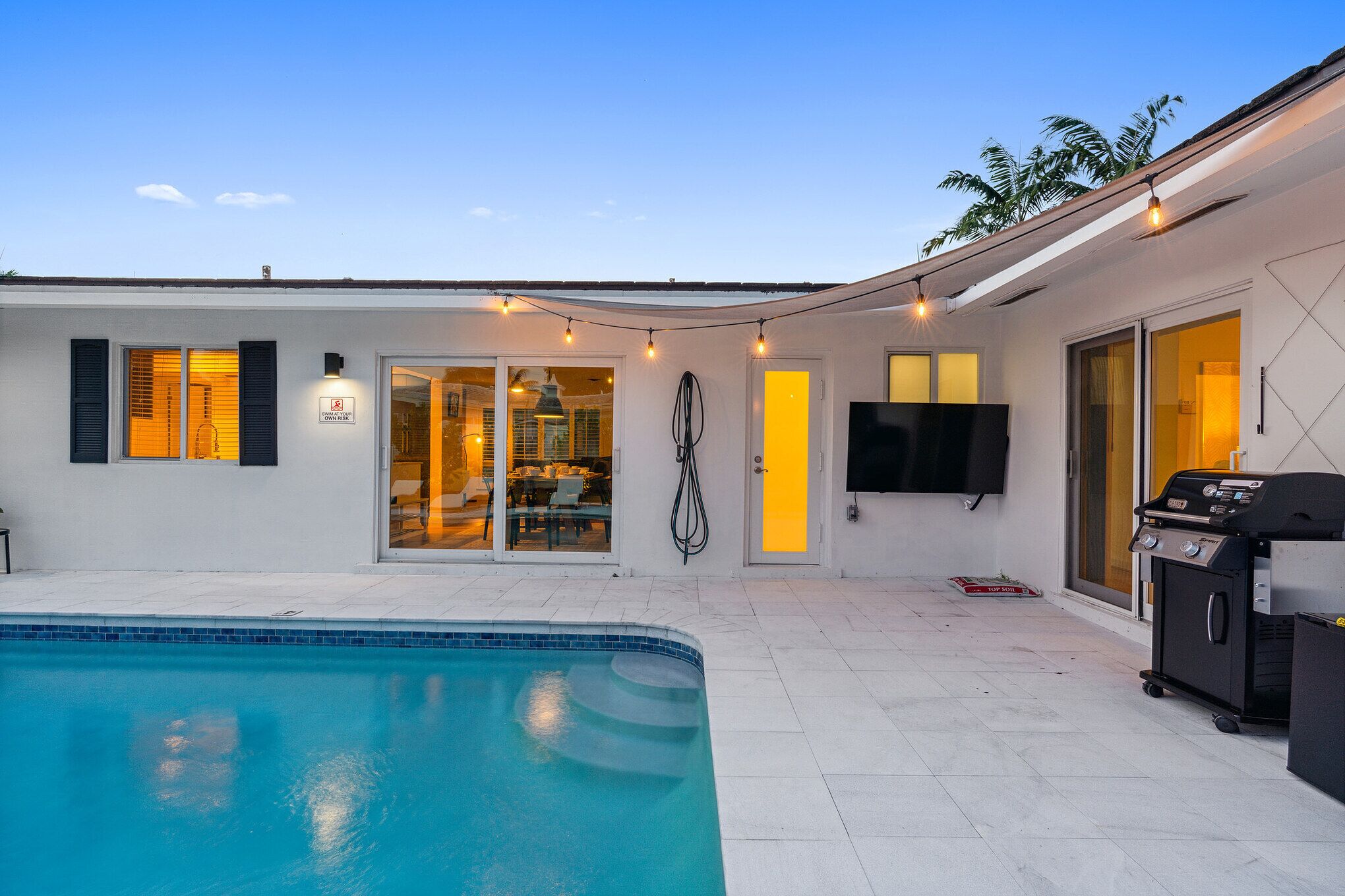 A poolside area with a swimming pool, a barbecue grill, and a dining area with glass doors.