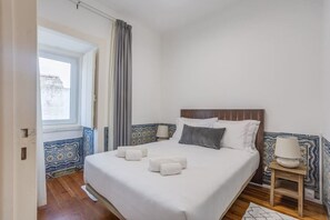 A bedroom with a bed, a nightstand, a window, and a view of the outside.