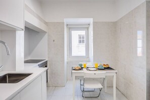 A compact kitchen with white cabinetry, a built-in sink, and a window above the dining table.