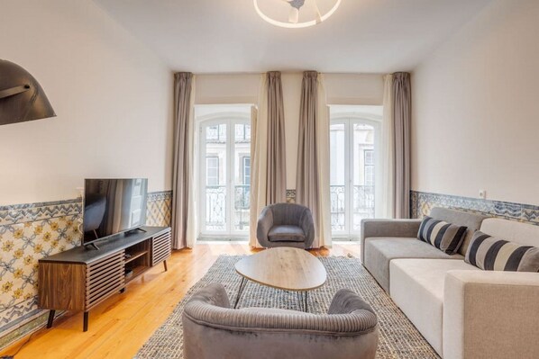 A living room with a TV, sofa, armchair, and a patterned rug.