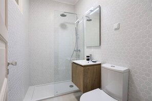 A bathroom with a glass shower enclosure, a wooden vanity, and a white toilet.