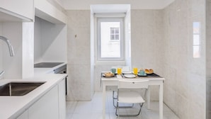 Una cocina compacta con muebles blancos, un lavamanos integrado y una ventana sobre la mesa de comedor.