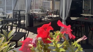 An outdoor seating area with tables and chairs, a white umbrella, and a building with balconies in the background.