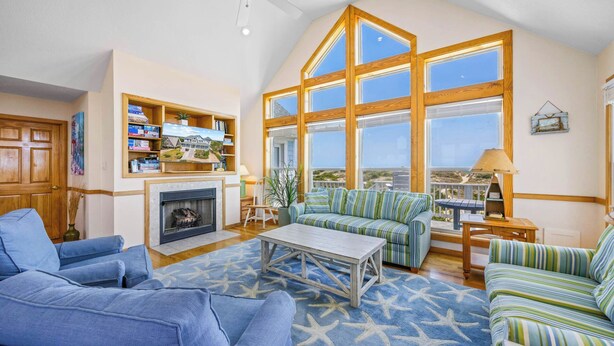 A spacious living room with a fireplace, large windows, and a view of the beach. - Premier Oceanfront Dog Friendly Home w/ Private Pool, Hot Tub, Game Room (Salvo)