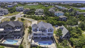 A residential area with houses, a swimming pool, and a large house with a balcony. - Premier Oceanfront Dog Friendly Home w/ Private Pool, Hot Tub, Game Room (Salvo)