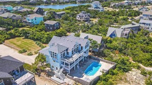 A large, multi-story house with a prominent balcony and a swimming pool, surrounded by lush greenery and a lake view. - Premier Oceanfront Dog Friendly Home w/ Private Pool, Hot Tub, Game Room (Salvo)