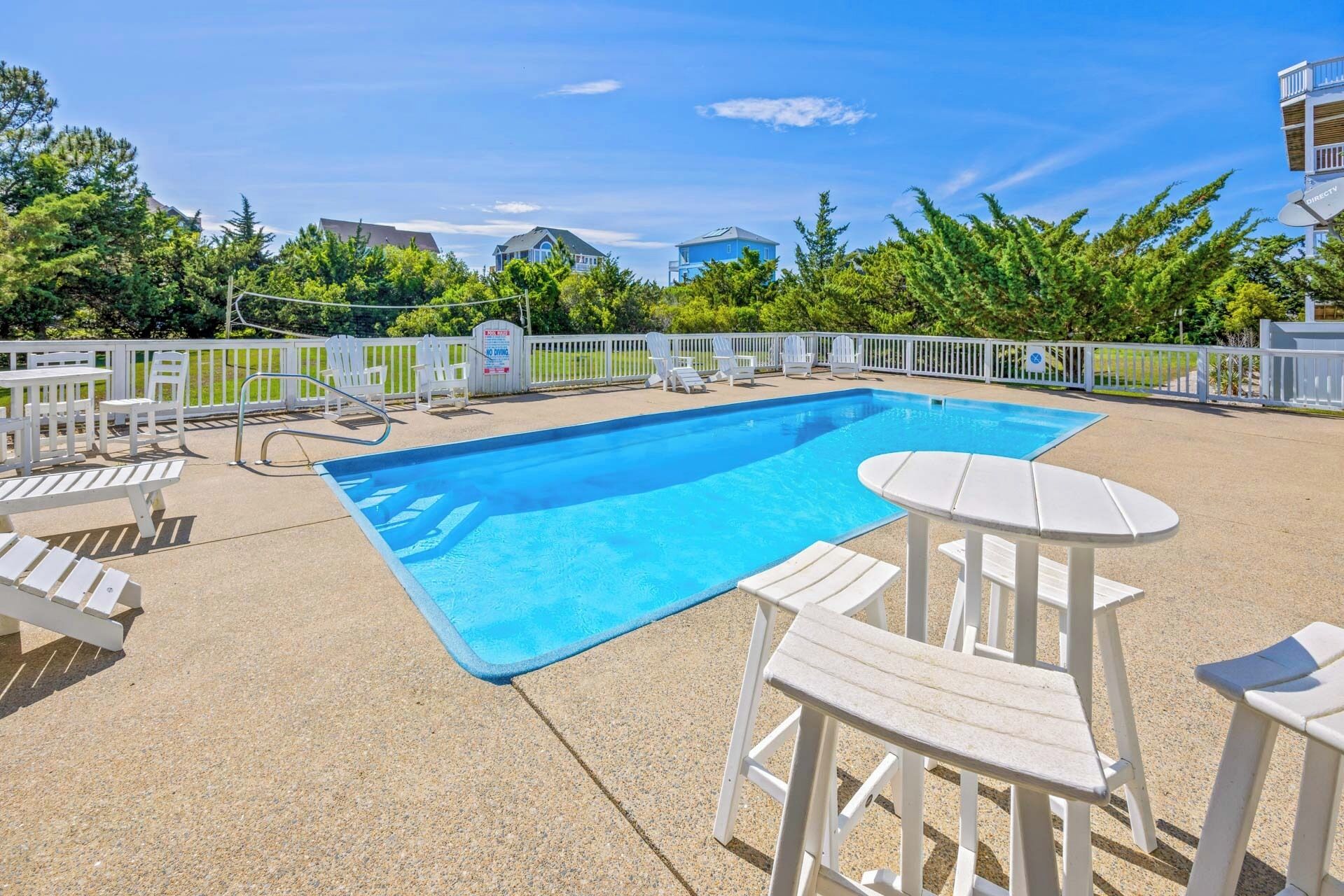 A rectangular pool with a white deck, surrounded by white chairs and tables.