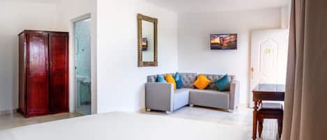 Een slaapkamer met een bed, een grijze bank met kleurrijke kussens, een houten garderobe, een televisie en een deur met het nummer 20.