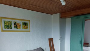 A bedroom with a bed, a chair, a nightstand, a picture frame, and a ceiling fan. - Appartement (Gueberschwihr)