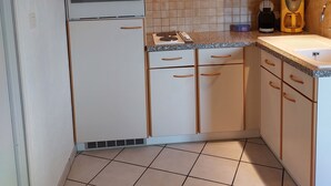 A compact kitchen with white cabinets, a built-in oven, a stove, and a coffee maker. - Appartement (Gueberschwihr)