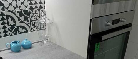 A kitchen with a grey countertop, a microwave, an oven, and a drawer with utensils.