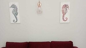A red sectional sofa against a white wall with two seahorse artwork pieces and a pendant light. - moon house (San Cesario di Lecce)