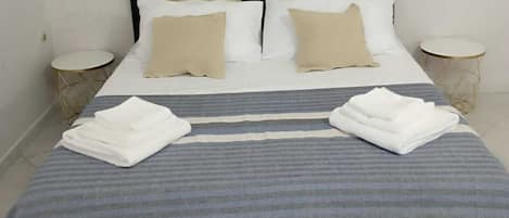 A neatly made bed with a striped blanket and two folded towels, a dark headboard, and a painting of a wave on the wall.