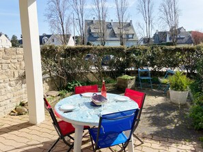 An outdoor patio with a round table set for dining, surrounded by red and blue chairs.