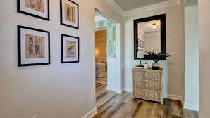 A hallway with framed architectural drawings on the wall, a wicker chest of drawers, and a mirror. - Family Oasis 1 block from the beach near Boardwalk (Carolina Beach)