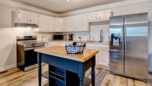 A modern kitchen with white cabinetry, stainless steel appliances, and a wooden island. - Family Oasis 1 block from the beach near Boardwalk (Carolina Beach)