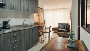 A modern kitchen with grey cabinets, a coffee maker, and a dining area with a wooden table and chairs. - Hermoso y Cómodo Apartamento en El Poblado!!! (Medellín)