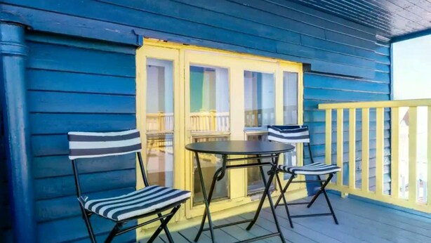 A covered outdoor seating area with a table and four striped chairs, a yellow railing, and a blue wooden deck. - Unique & Sunny Top Floor Old Quebec Gem (Québec City)