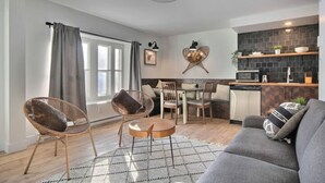 A modern living room with a grey sofa, two wicker chairs, a round coffee table, and a dining area with a wooden table and chairs. - Unique & Sunny Top Floor Old Quebec Gem (Québec City)