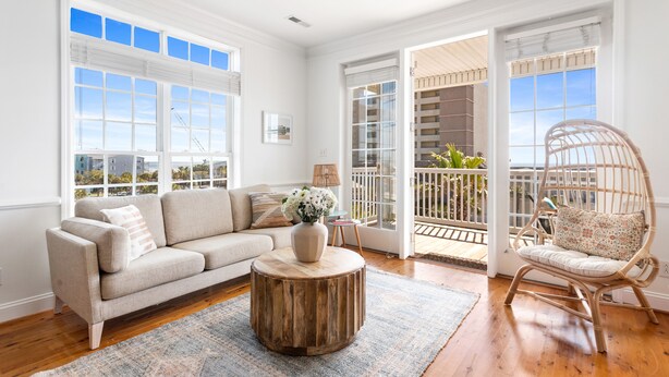 Un salón espacioso con un sofá color beige, una mesa de centro redonda de madera y una silla de mimbre.