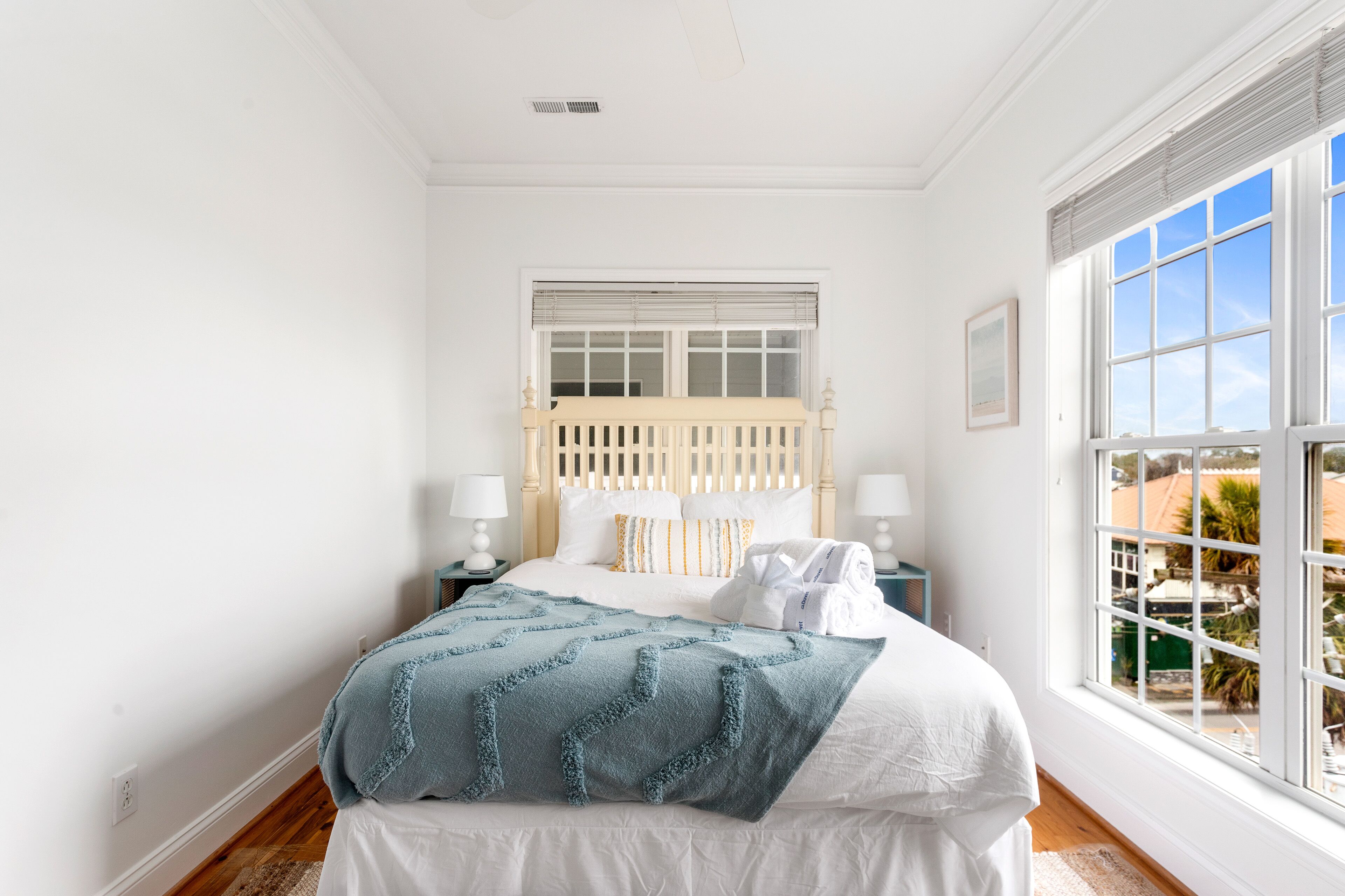 Une chambre avec un grand lit, des murs blancs, une fenêtre avec des stores et une vue sur les bâtiments environnants.