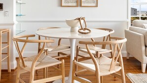 Un comedor con una mesa redonda, seis sillas de mimbre y dos cuadros enmarcados en la pared.