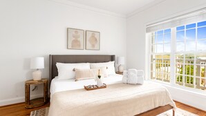 Un dormitorio con una cama grande, dos mesitas de noche, un ventanal con vistas y una obra de arte en la pared.