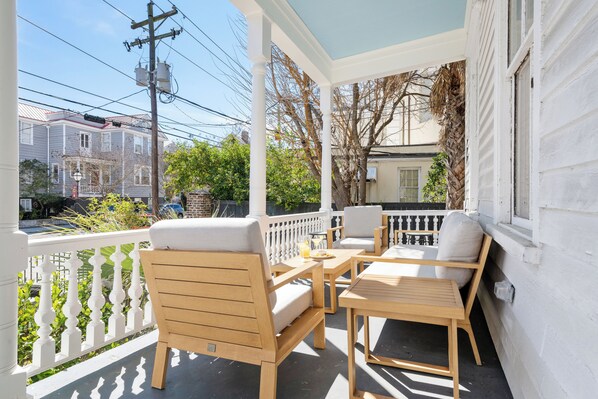 A covered porch with wooden furniture and a view of neighboring houses.