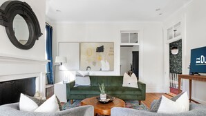 Una sala de estar con un sofá verde, dos sillones grises, una mesa de centro de madera y una chimenea.