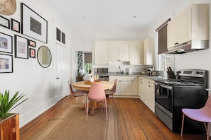 A kitchen with white cabinets, a black stove, and a dining area with pink chairs.