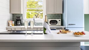 Een keuken met een wit aanrecht, een magnetron, een koelkast en een raam met uitzicht op bomen.