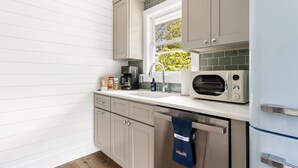 Een moderne keuken met witte kasten, een magnetron, een koffiezetapparaat en een raam met uitzicht op groen.