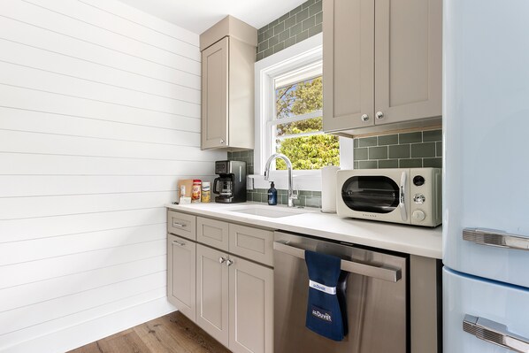 Una cocina moderna con armarios blancos, microondas, cafetera y ventana con vista a follaje.