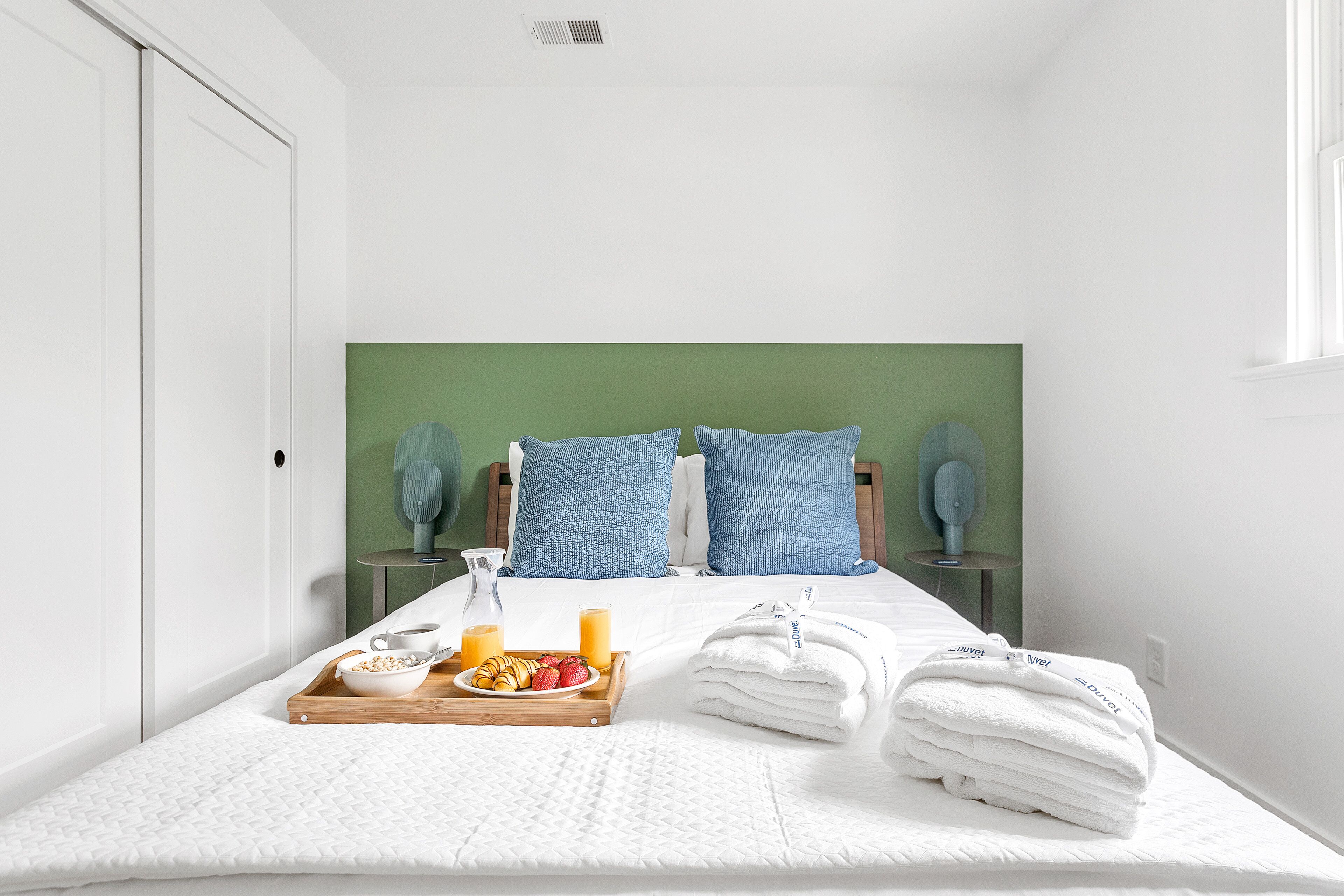 A hotel room with a bed, pillows, a bedside table, a tray with breakfast, and a window.